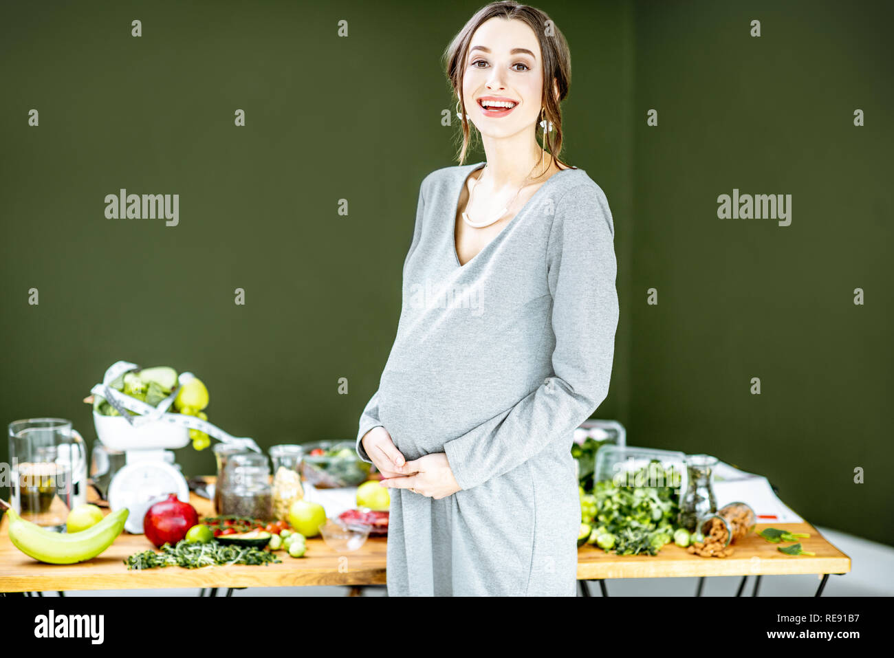 Bella donna incinta con vario di cibo sano sullo sfondo verde. Mangiare sano e benessere durante il concetto di gravidanza Foto Stock