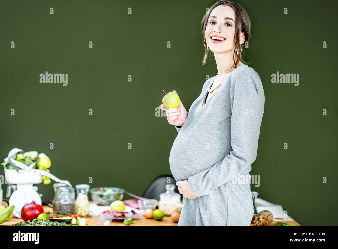 Bella donna incinta con vario di cibo sano sullo sfondo verde. Mangiare sano e benessere durante il concetto di gravidanza Foto Stock