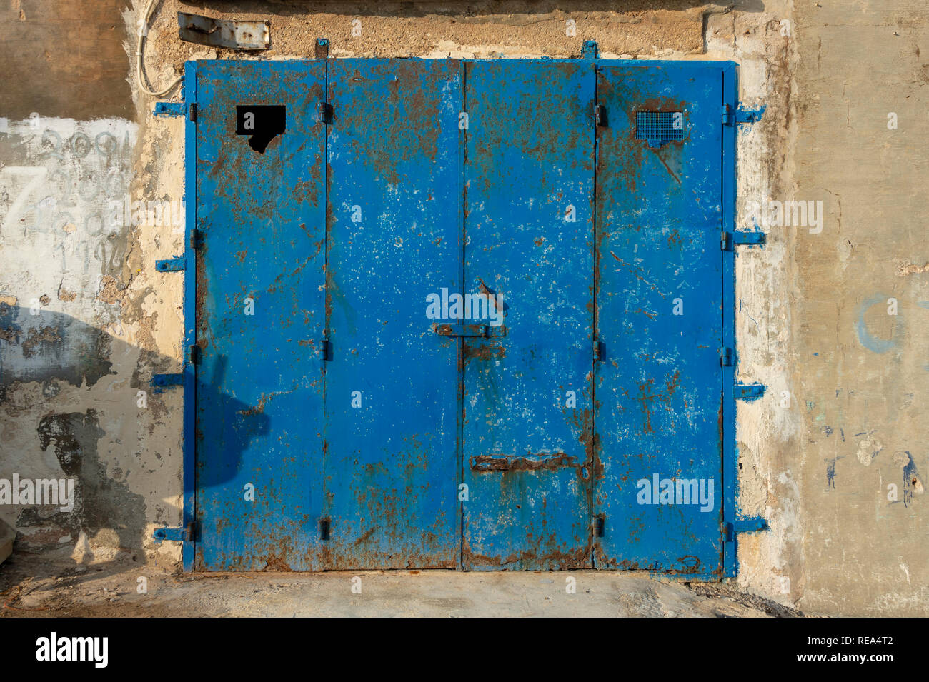 Rusty in metallo blu porta di garage in un weatherbeaten muro di pietra Foto Stock