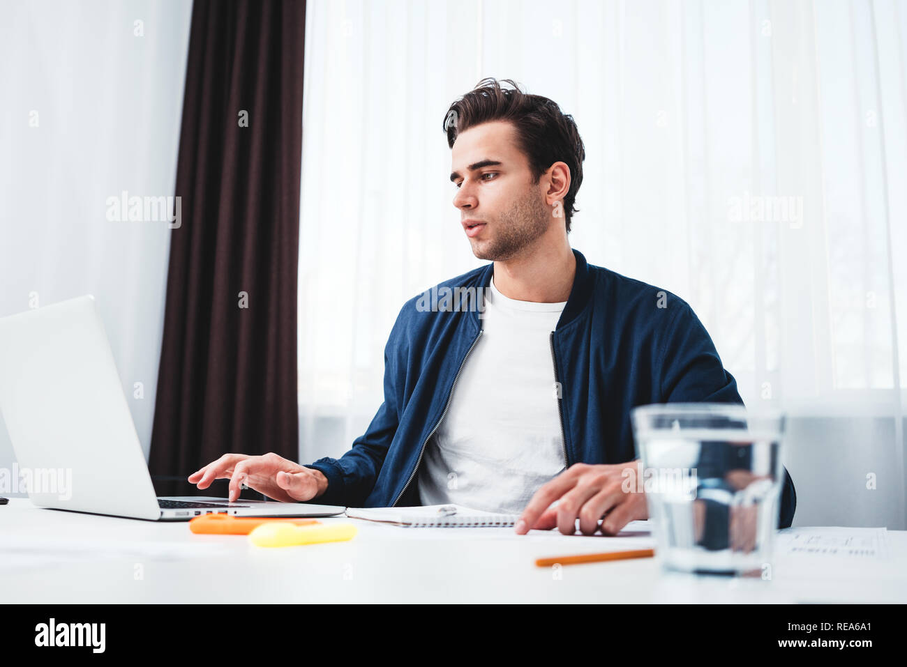 Concentrate l uomo la scrittura di nuove idee in notepad guardando sullo schermo portatile. Giovane collega che siede a tavola e lavoro in ufficio Foto Stock