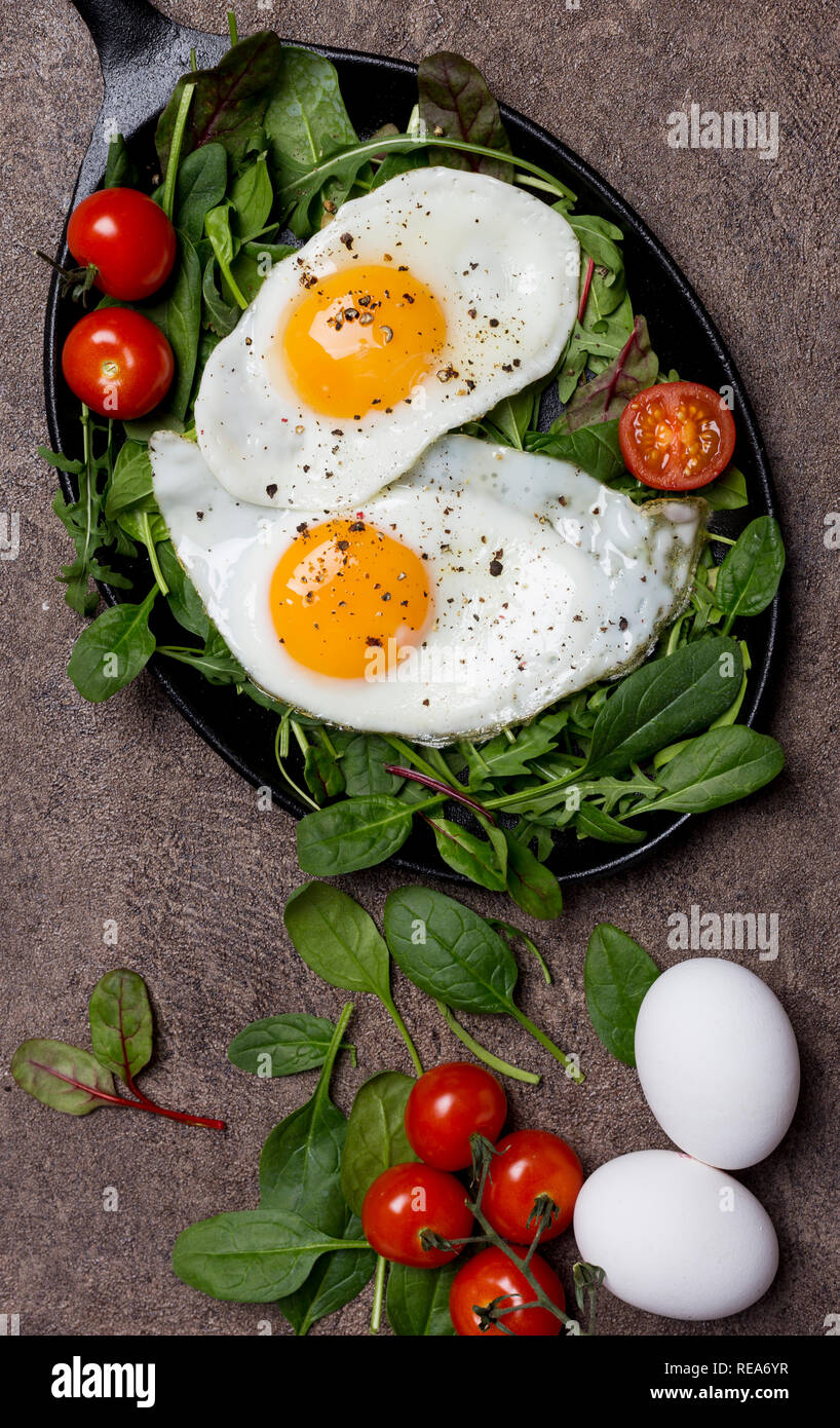 Uova fritte con erbe fresche e pomodorini al pan per la prima colazione, su sfondo marrone. Concetto di gustosa e uno stile di vita sano Foto Stock