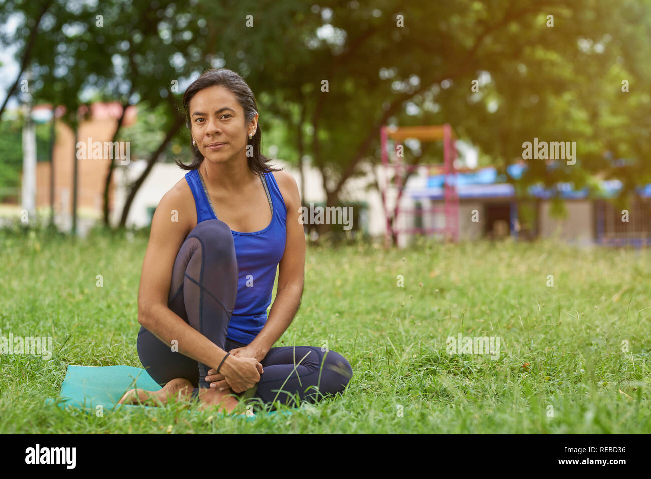 Giovane donna yoga trainer sedersi sul tappeto in estate sfondo parco Foto Stock
