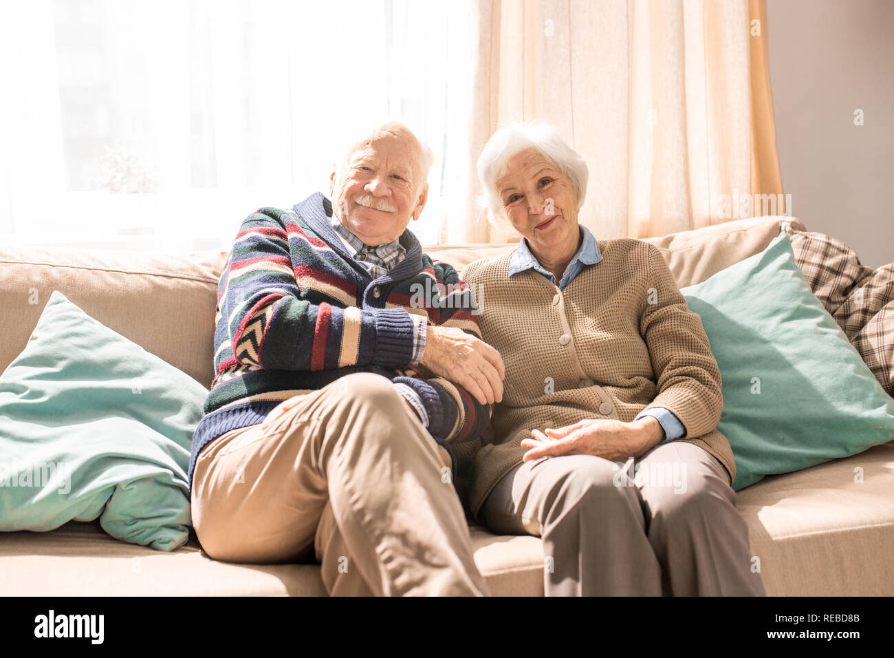 Ritratto di amorevole coppia senior in posa insieme sorridente in telecamera comodamente seduti sul divano di casa illuminata dalla luce del sole, spazio di copia Foto Stock