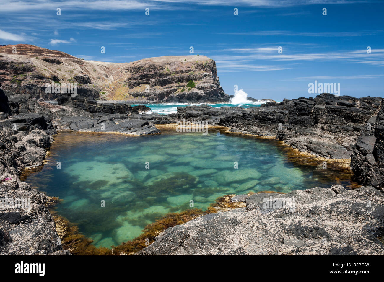 Rock pool in primo piano con onde che si infrangono da l'oceano sullo sfondo, Bushrangers Bay, Victoria Australia Foto Stock