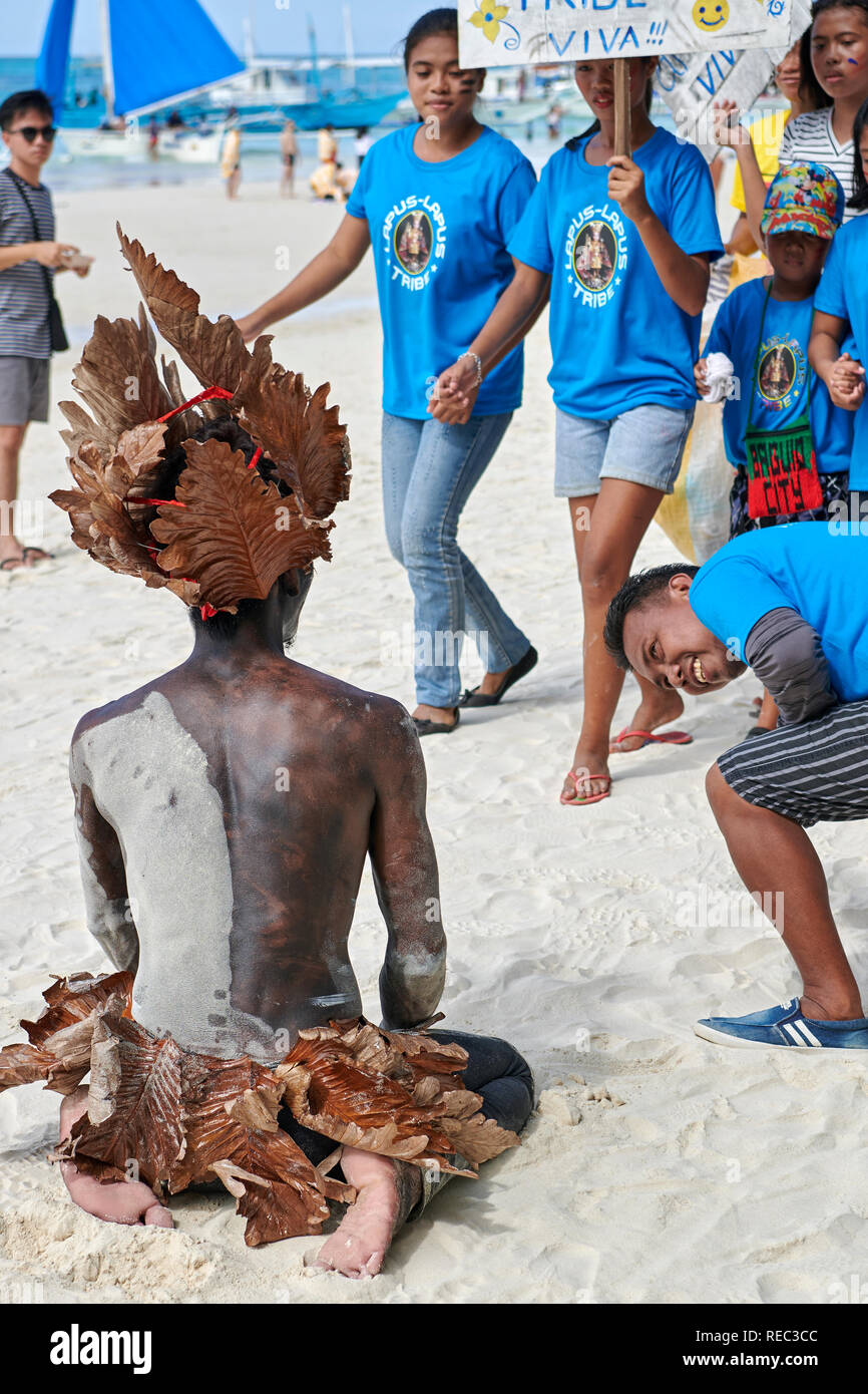 Un gruppo di giovani residenti locali è eccitante di un altro partecipante ubriaco vestito di foglie di pianta al Ati-Atihan Parade lungo la spiaggia Bianca di Boracay. Foto Stock