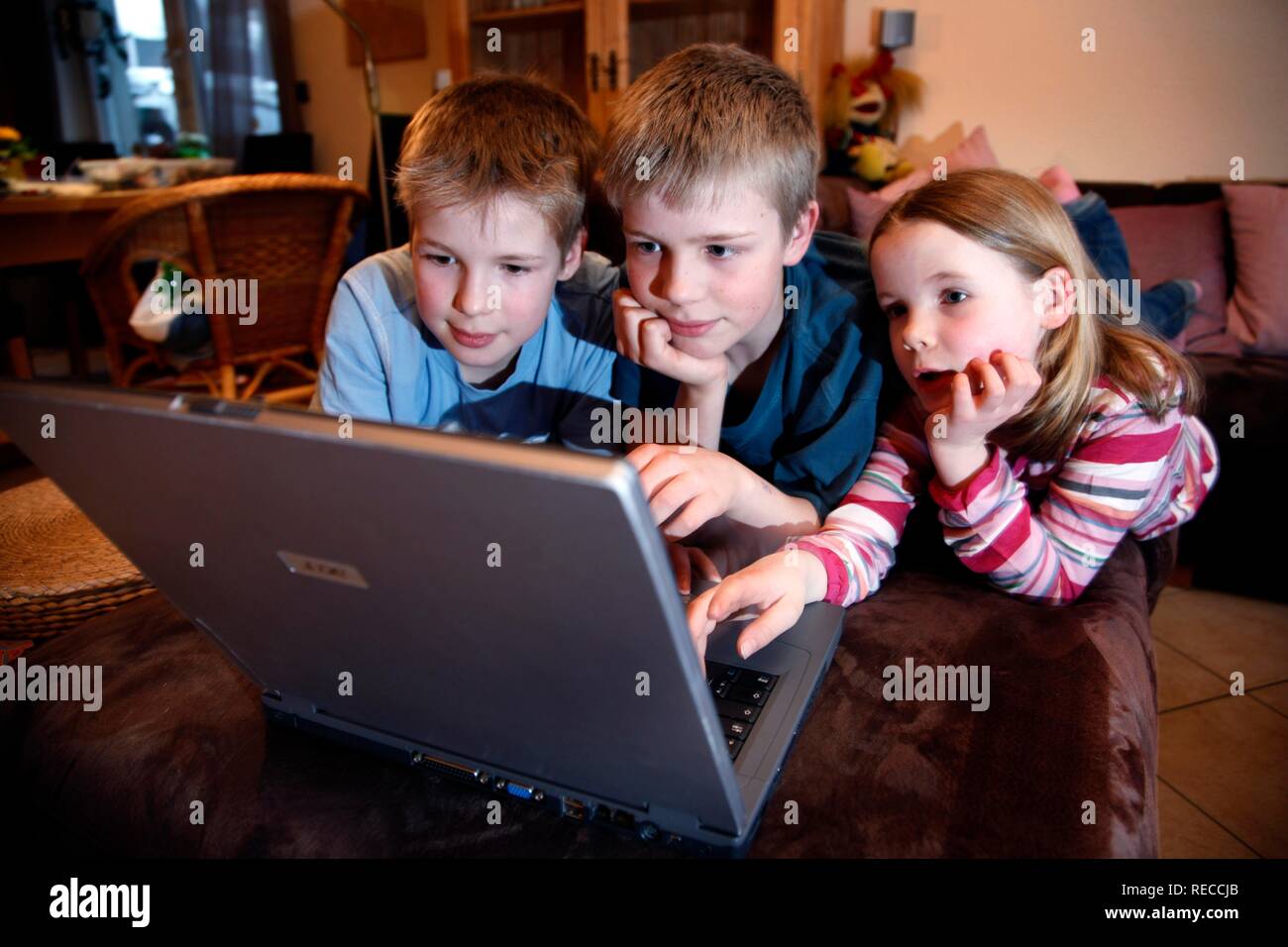 Fratelli, 7, 11, 13 anni, con computer portatile, nel soggiorno, la riproduzione di un gioco educativo quiz Foto Stock