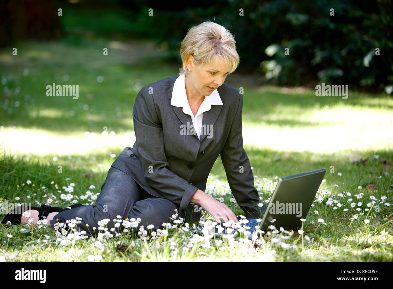 Donna che indossa un ladies suit, pantaloni adatti, imprenditrice, inizio 40s, lavorando sul suo computer portatile in un parco Foto Stock