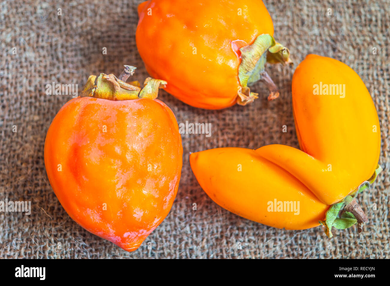 Close up vista dall'alto di arancia cachi frutta conservata su un tappeto di iuta. Un frutto ha una forma unica Foto Stock