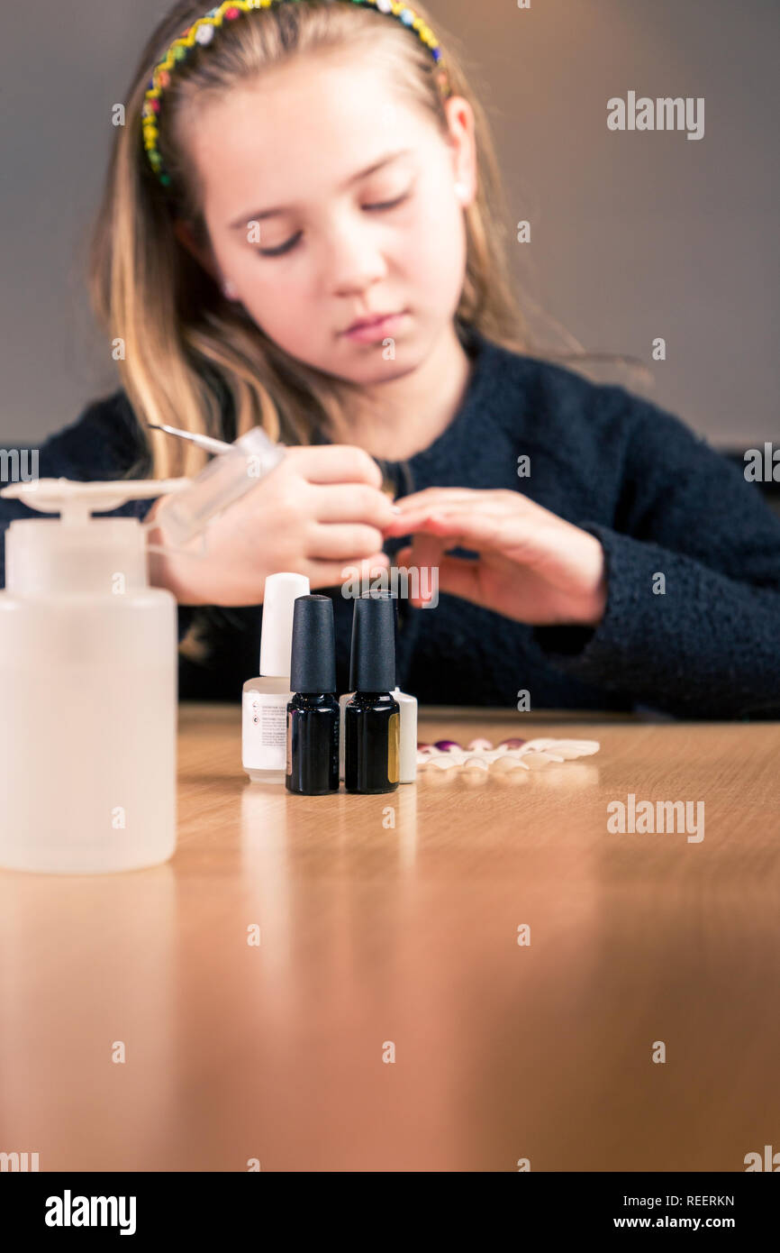 Set di strumenti di personalizzazione per manicure sul tavolo della cucina mentre la ragazza è con lima per unghie. profondità di campo, concentrarsi su smalto per unghie bottiglie Foto Stock