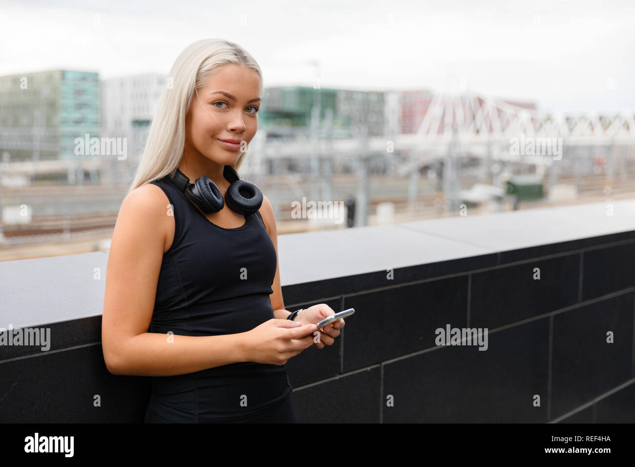 Montare sorridente atleta femminile con le cuffie e Smartwatch in città Foto Stock