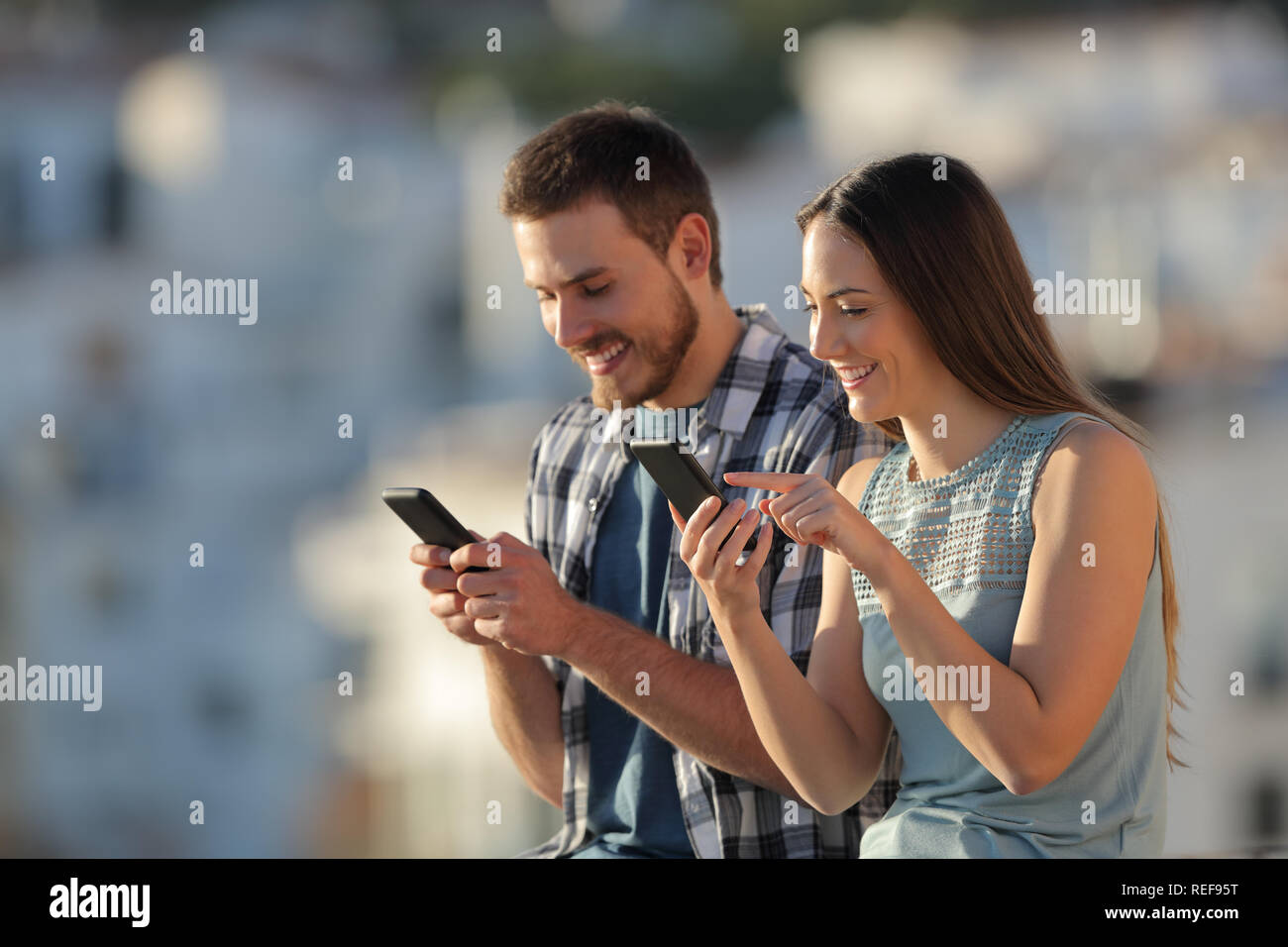 Felice coppia utilizzando i loro smart phone all'aperto in una città al tramonto Foto Stock