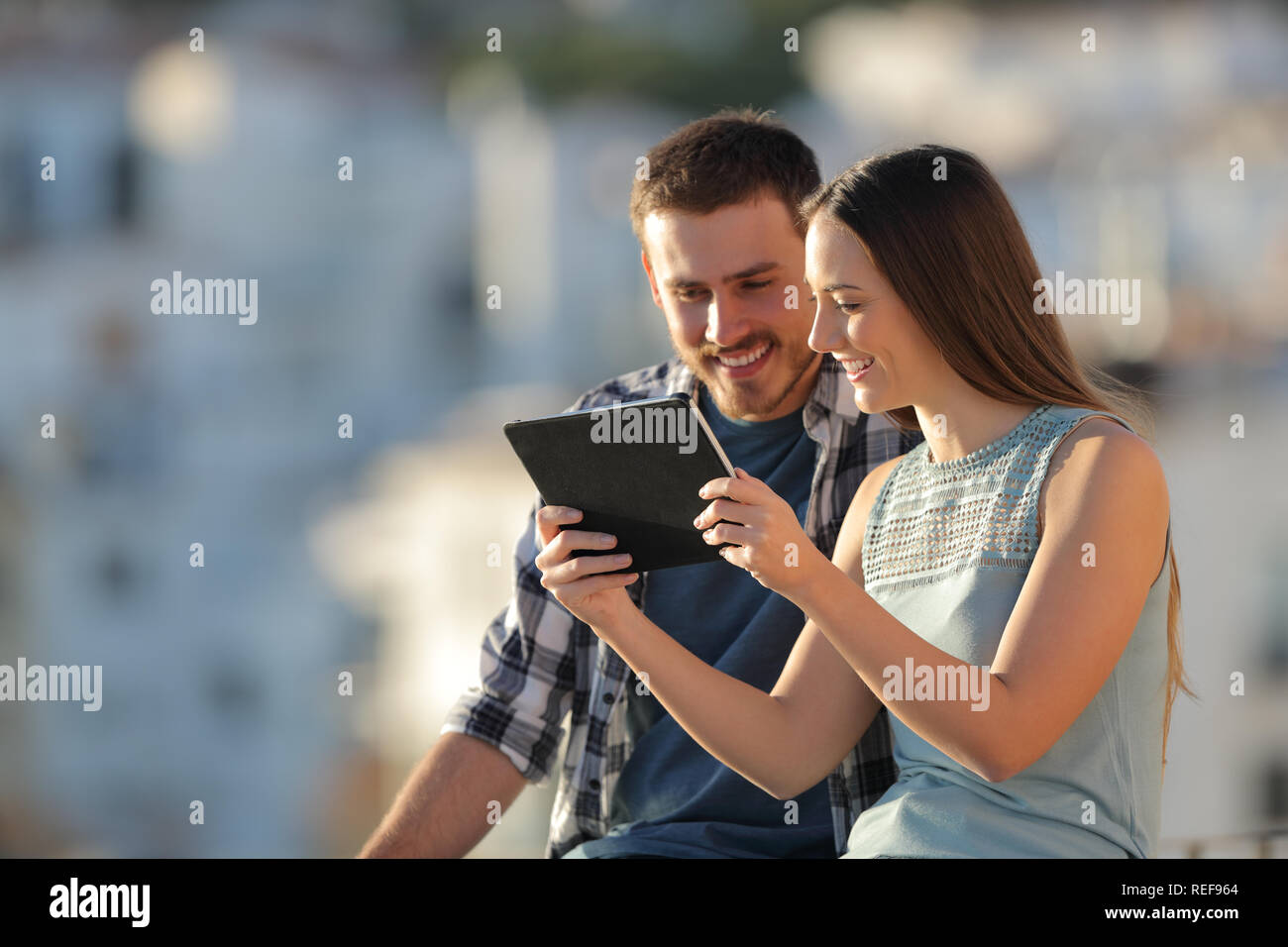 Coppia felice guardando tablet contenuto all'aperto in una città in periferia al tramonto Foto Stock