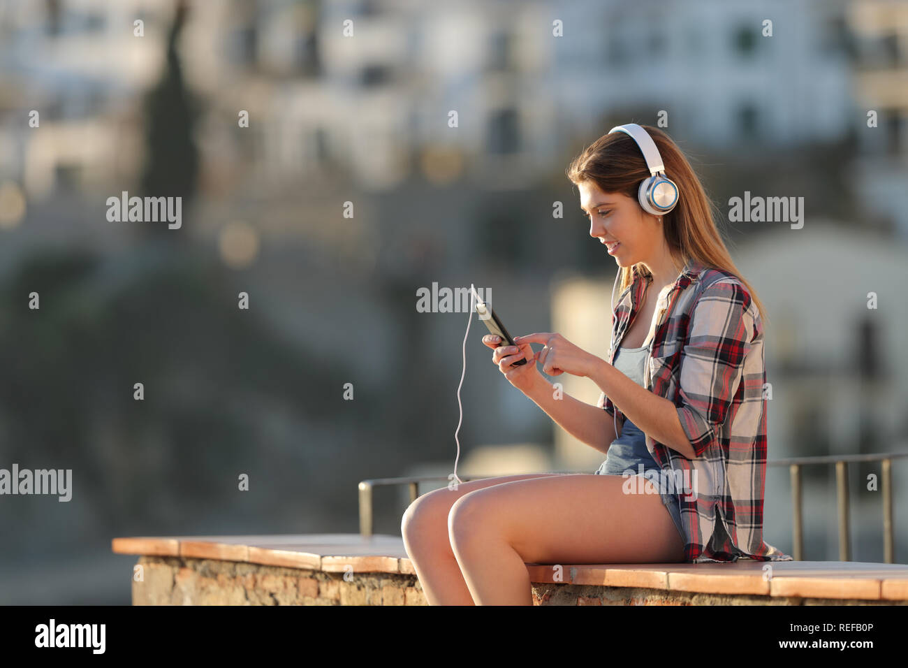 Teen ascoltando musica su smart phone all'aperto in una città in periferia al tramonto Foto Stock