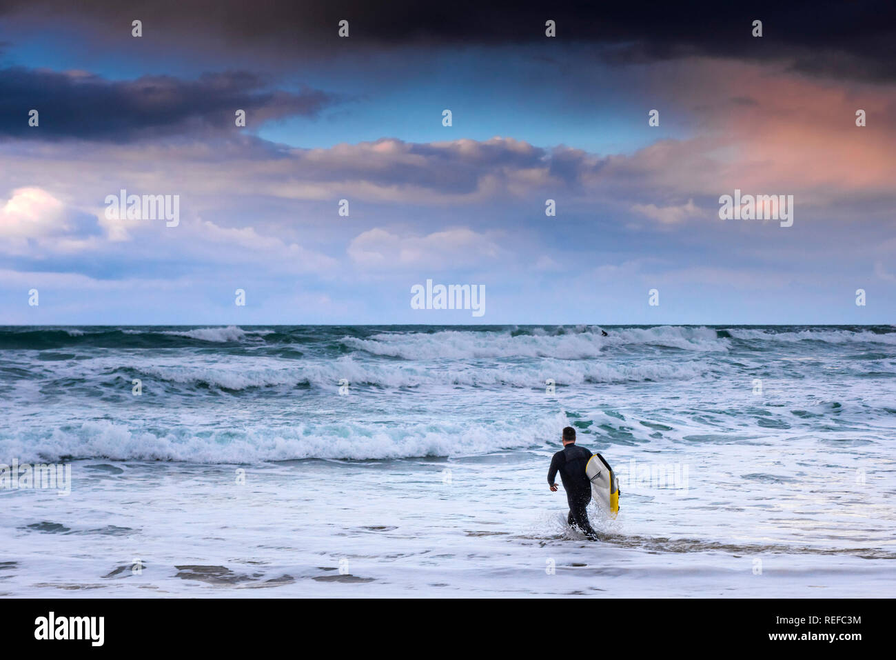 Bellissimi colori pastello nel cielo come il sole tramonta su un lone surfer a piedi in mare a Fistral Beach in Newquay Cornwall. Foto Stock