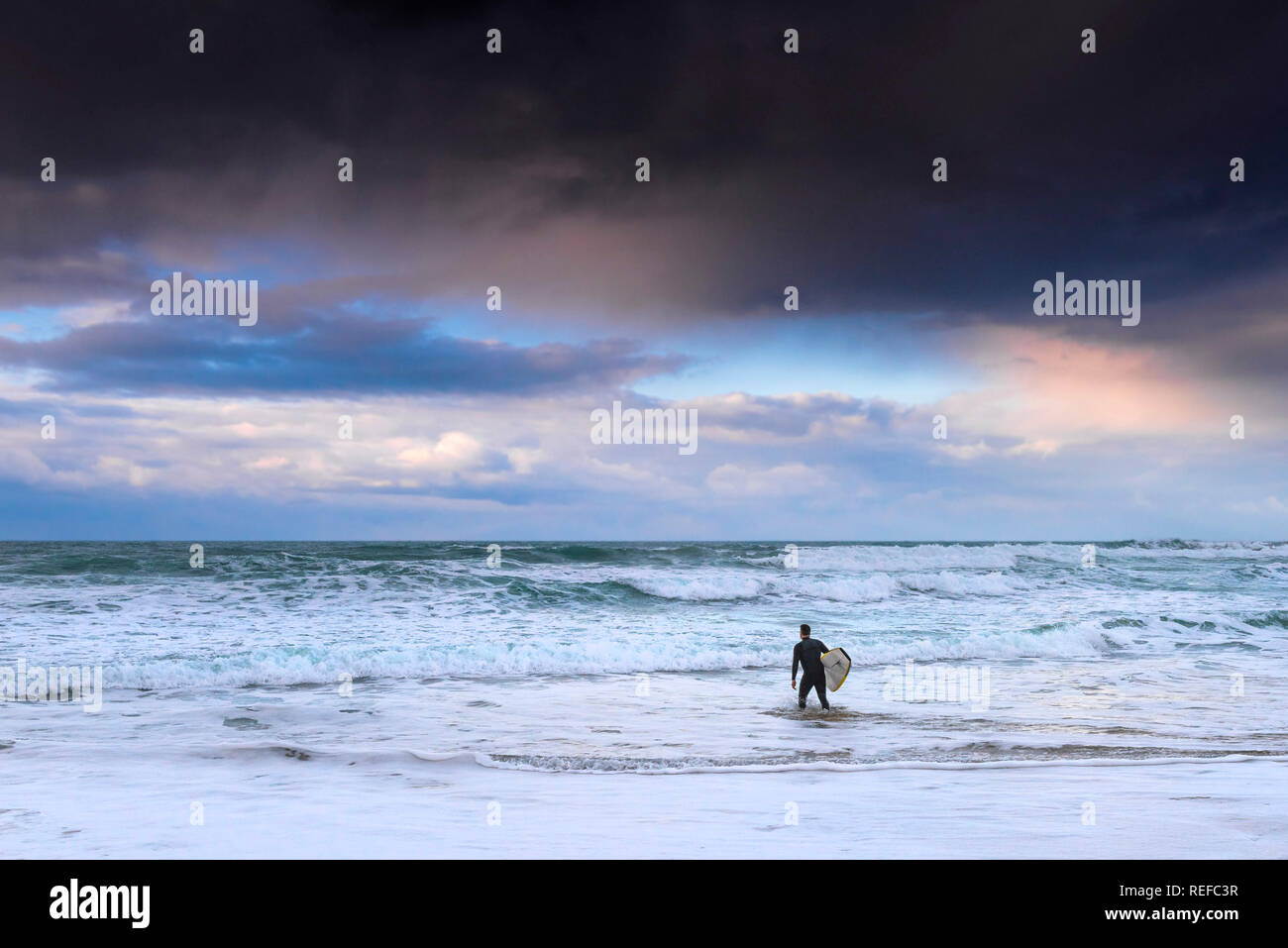 Bellissimi colori pastello nel cielo come il sole tramonta su un lone surfer a piedi in mare a Fistral Beach in Newquay Cornwall. Foto Stock