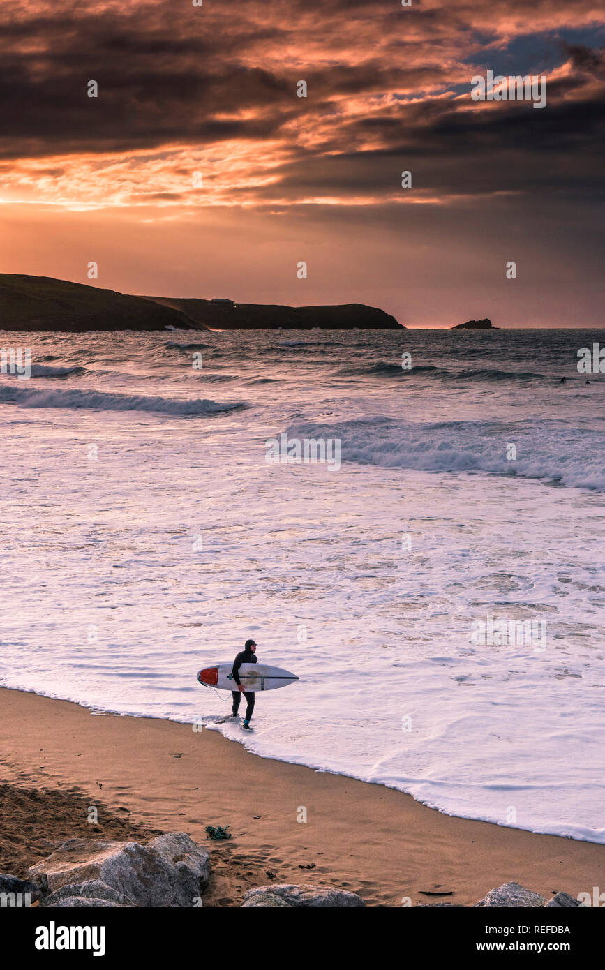 Un tramonto spettacolare come lone surfer portando la sua tavola da surf a piedi lungo il litorale di Fistral Beach in Newquay Cornwall. Foto Stock