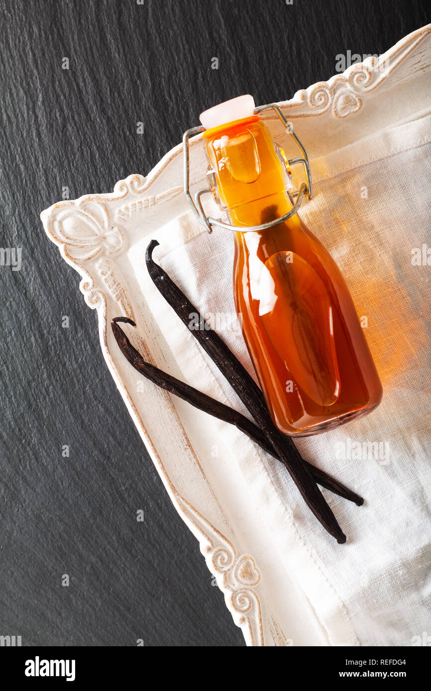 In casa di estratto di vaniglia in una bottiglia di vetro e baccelli di vaniglia su sfondo nero con spazio di copia Foto Stock