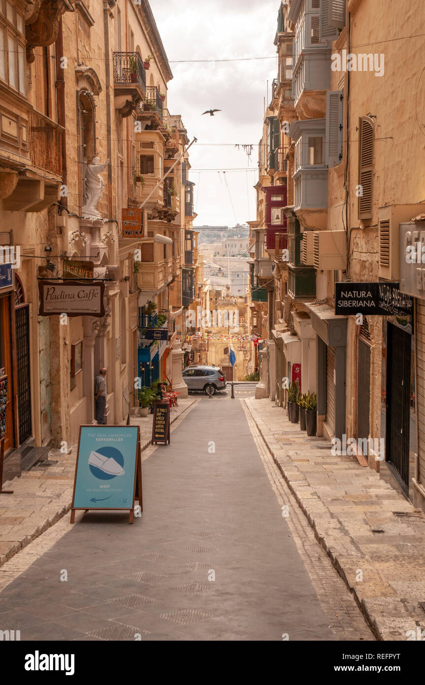 Una vista verso il basso St. Lucia Street. Si tratta di una tipica stradina secondaria di negozi e residenze nel centro di La Valletta, la capitale di murata di Malta. Foto Stock