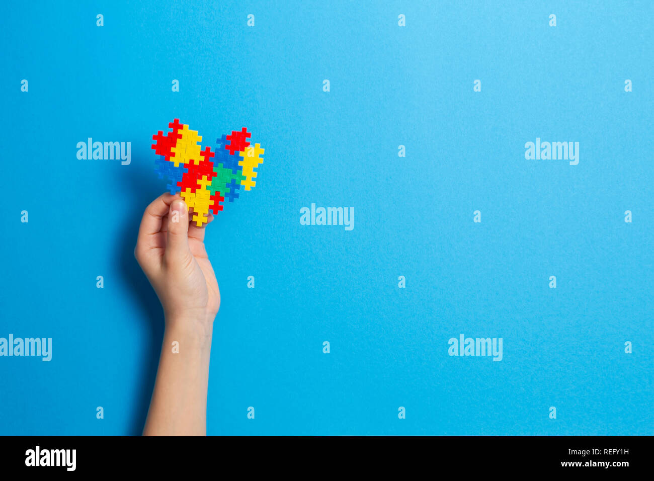Bambino mano azienda cuore colorati su sfondo blu. Mondo autismo consapevolezza giorno di concetto Foto Stock