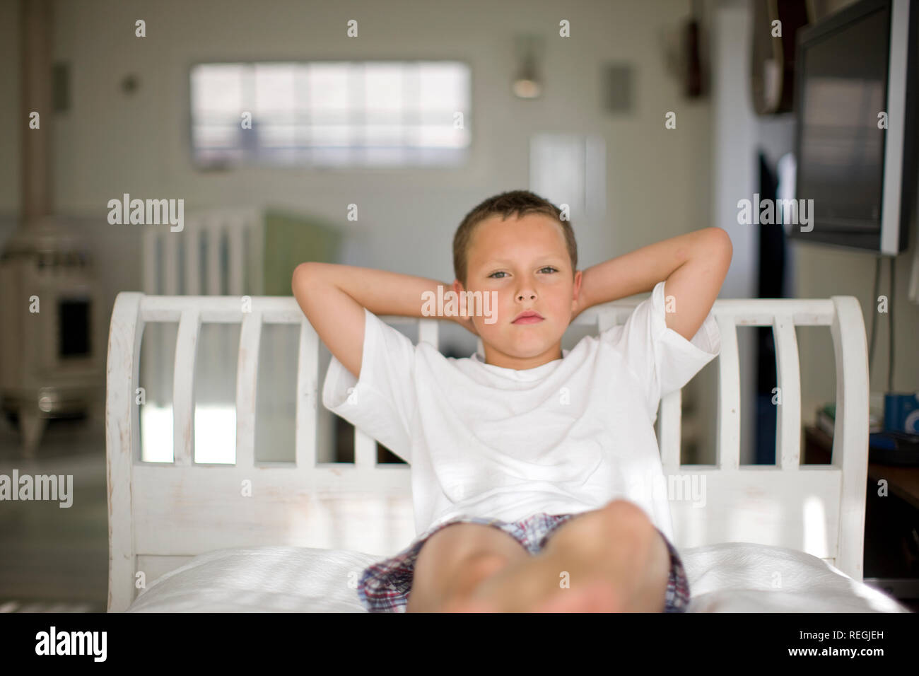 Ritratto di un ragazzo serio seduta su di un letto con le braccia dietro la sua testa. Foto Stock