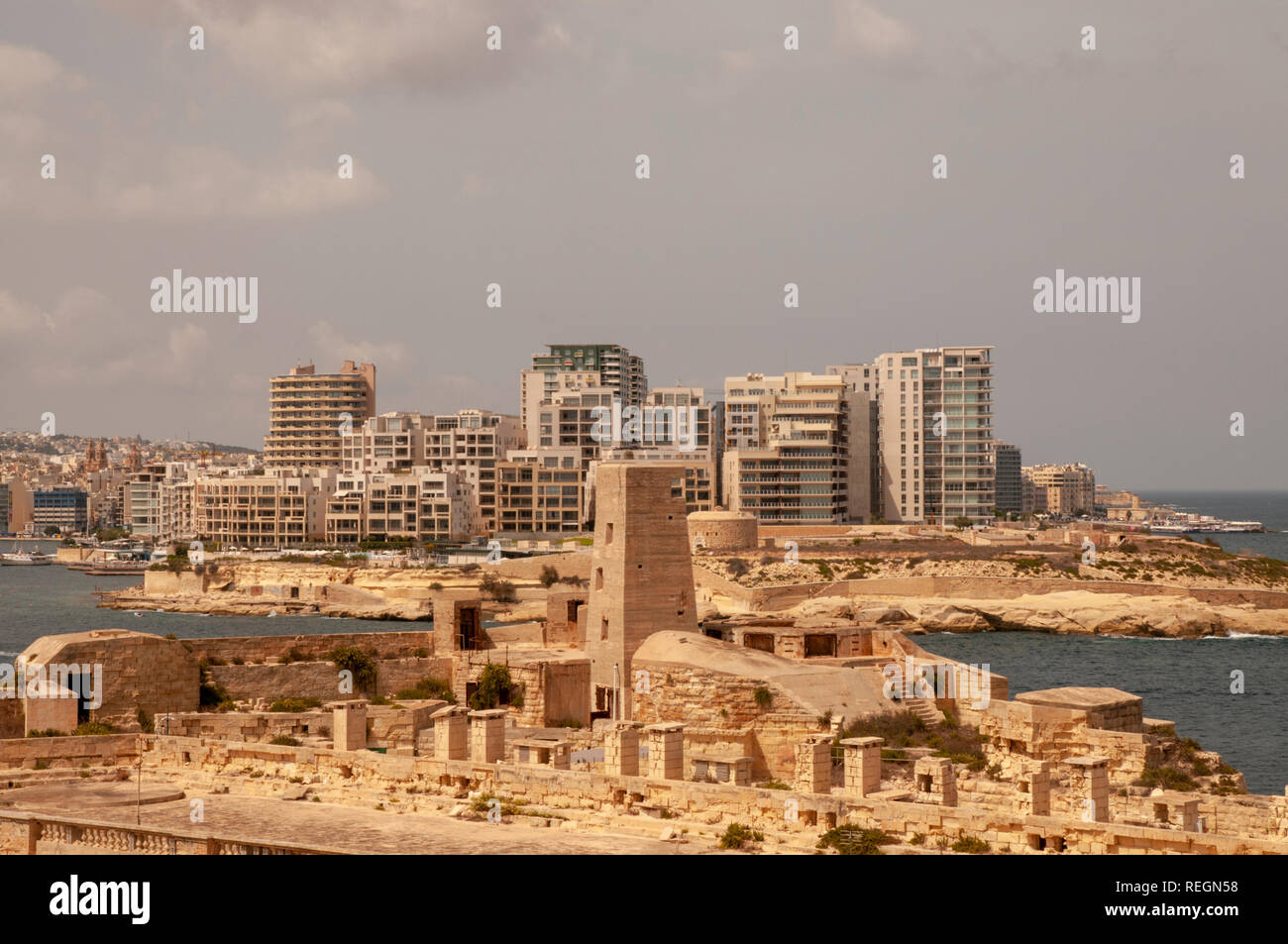 Edificio alto e moderno di edifici in Sliema seduta tutta la retta da La Valletta, Malta, con parte di Fort St Elmo in primo piano. Foto Stock