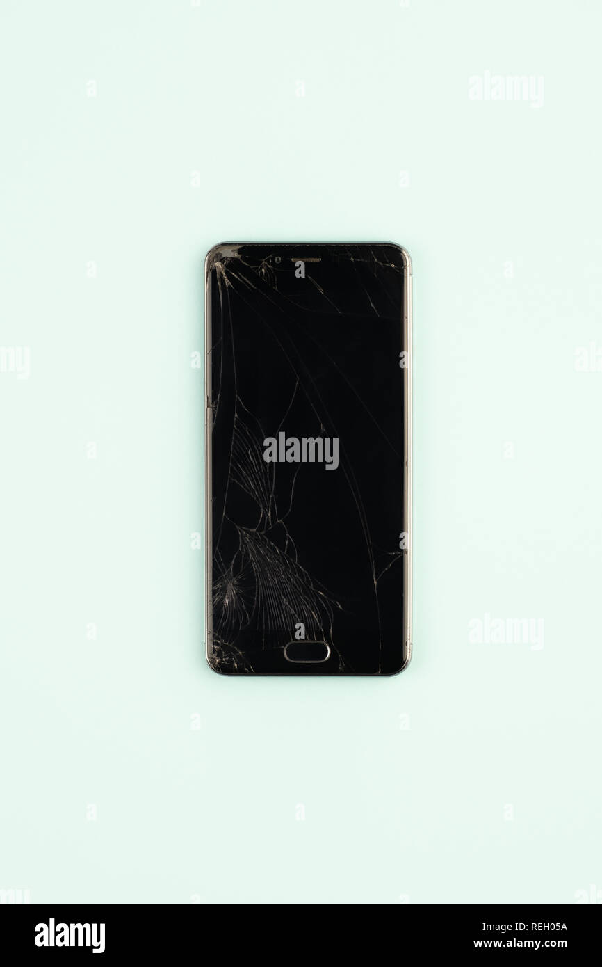 Telefono cellulare con rotture di schermo nero, vista dall'alto. Addolorato danneggiato lo smartphone nel verde pallido sfondo, colpo verticale Foto Stock