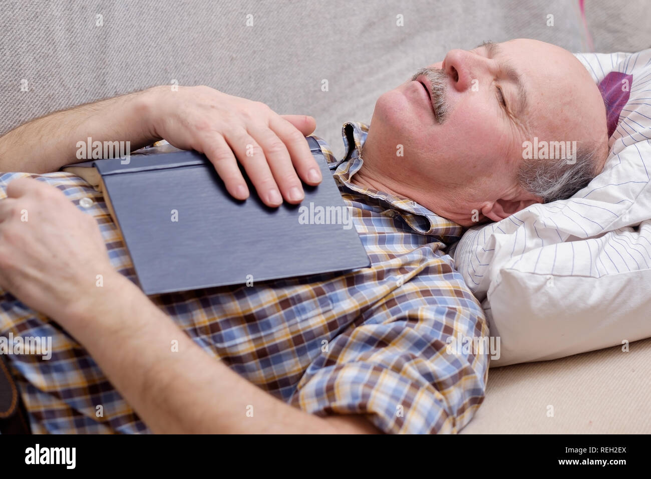 Senior uomo dorme sul divano con un libro Foto Stock