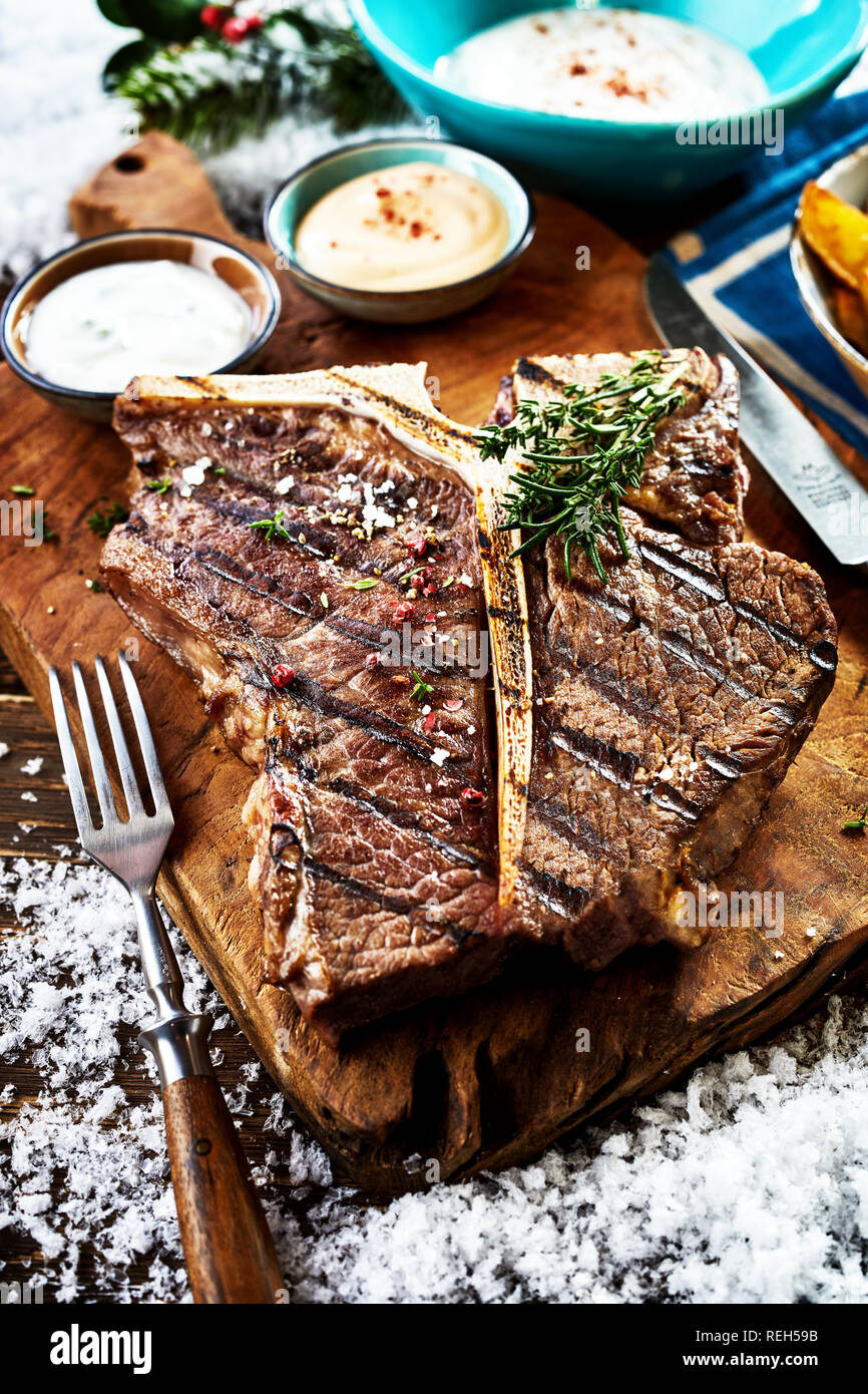 Vista ravvicinata di grigliate di t-bone steak con salse e piatti laterali sul tavolo Foto Stock