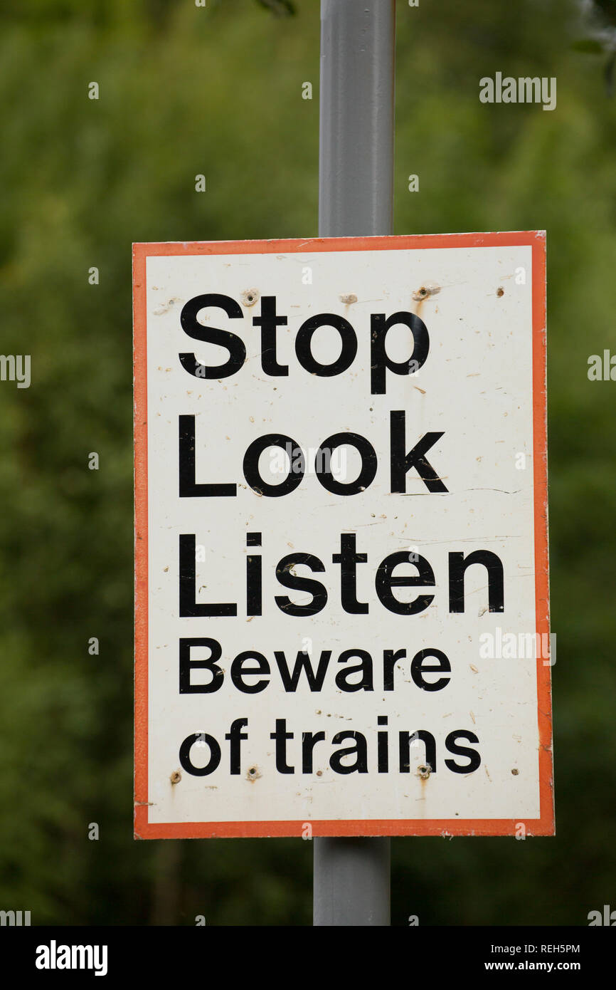 Un segno attenzione a guardare e ascoltare per treni accanto a un sentiero che attraversa una linea ferroviaria. Silverdale, Lancashire England Regno Unito GB Foto Stock