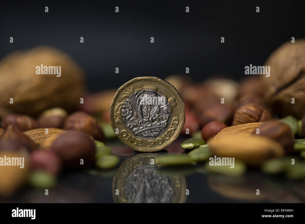 Una lira sterlina inglese coin circondato con varietà di dadi, comprese le noci, le nocciole, le mandorle e i semi di zucca in sfondo nero Foto Stock