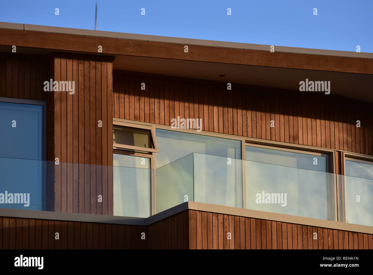 Facciata con finestre e veranda della moderna casa in legno con verticale di rivestimento verniciato e trasparente come il vetro ringhiera. Foto Stock