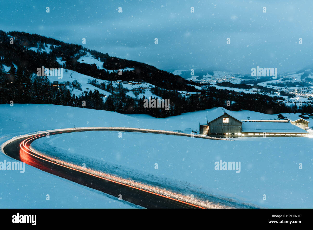 A lungo esposto notte fotografia di vetture di guidare attraverso una montagna innevata strada nelle Alpi dell'Austria. Foto Stock