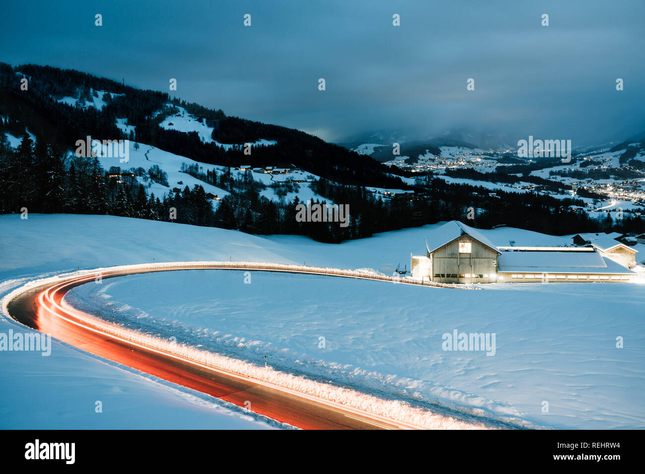 A lungo esposto notte fotografia di vetture di guidare attraverso una montagna innevata strada nelle Alpi dell'Austria. Foto Stock