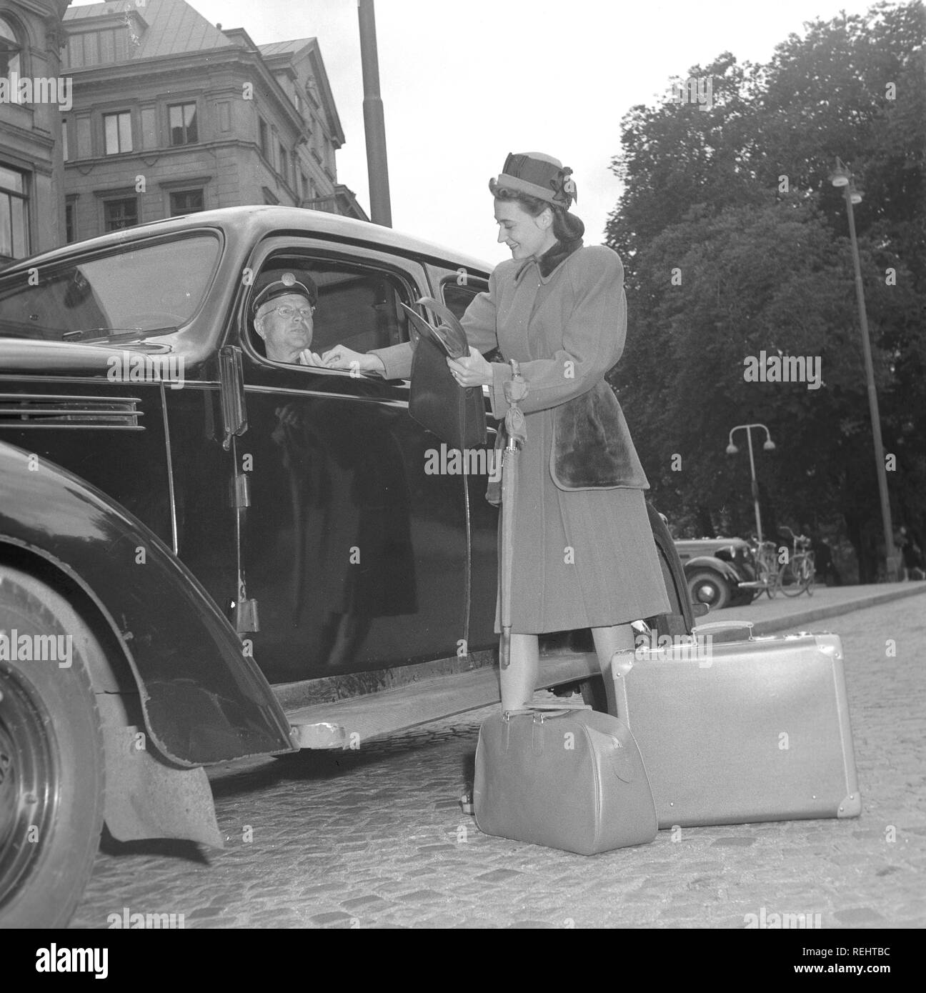 Le donne della moda nel 1940s. Una giovane donna in un tipico degli anni quaranta cappotto. Lei ha appena uscito da un taxi e paga il conducente. Foto Kristoffersson Ref V77-3. La Svezia 1947 Foto Stock