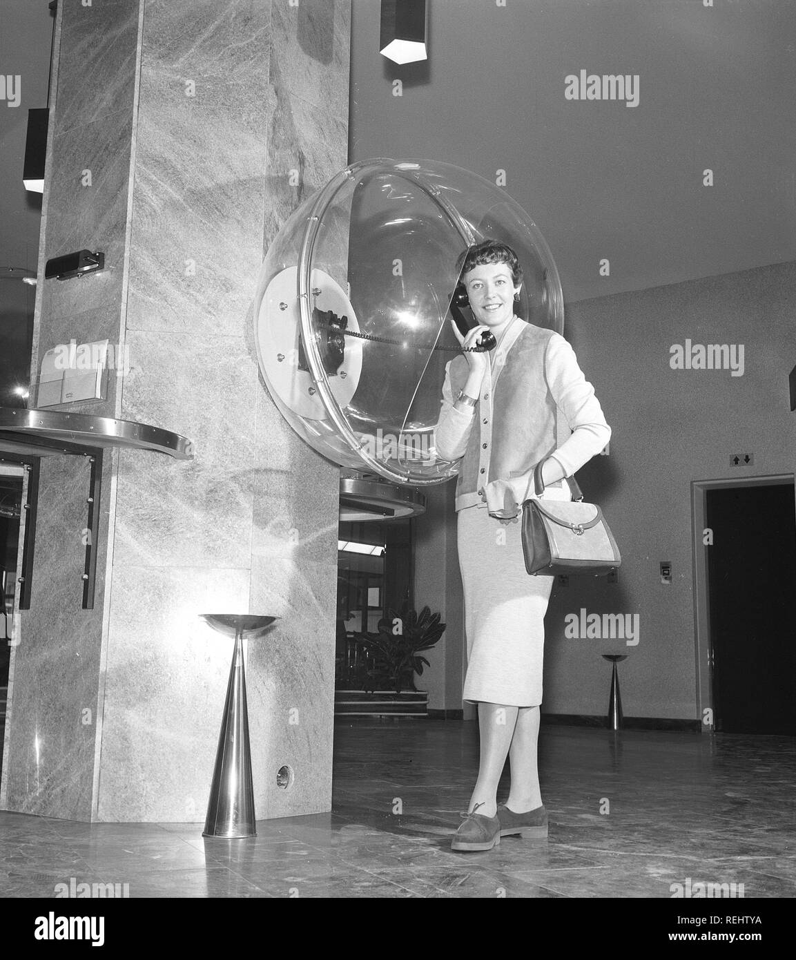 Telefono negli anni cinquanta. Una giovane donna è in piedi vestito in un tipico 50s abito e avente una conversazione telefonica in Palace Hotel di Stoccolma. La Cupola acrilica è un design funzionale nel caso in cui la persona che parla, non essendo intercettate da qualcuno. La Svezia degli anni cinquanta. Foto Kristoffersson ref CB23-2 Foto Stock