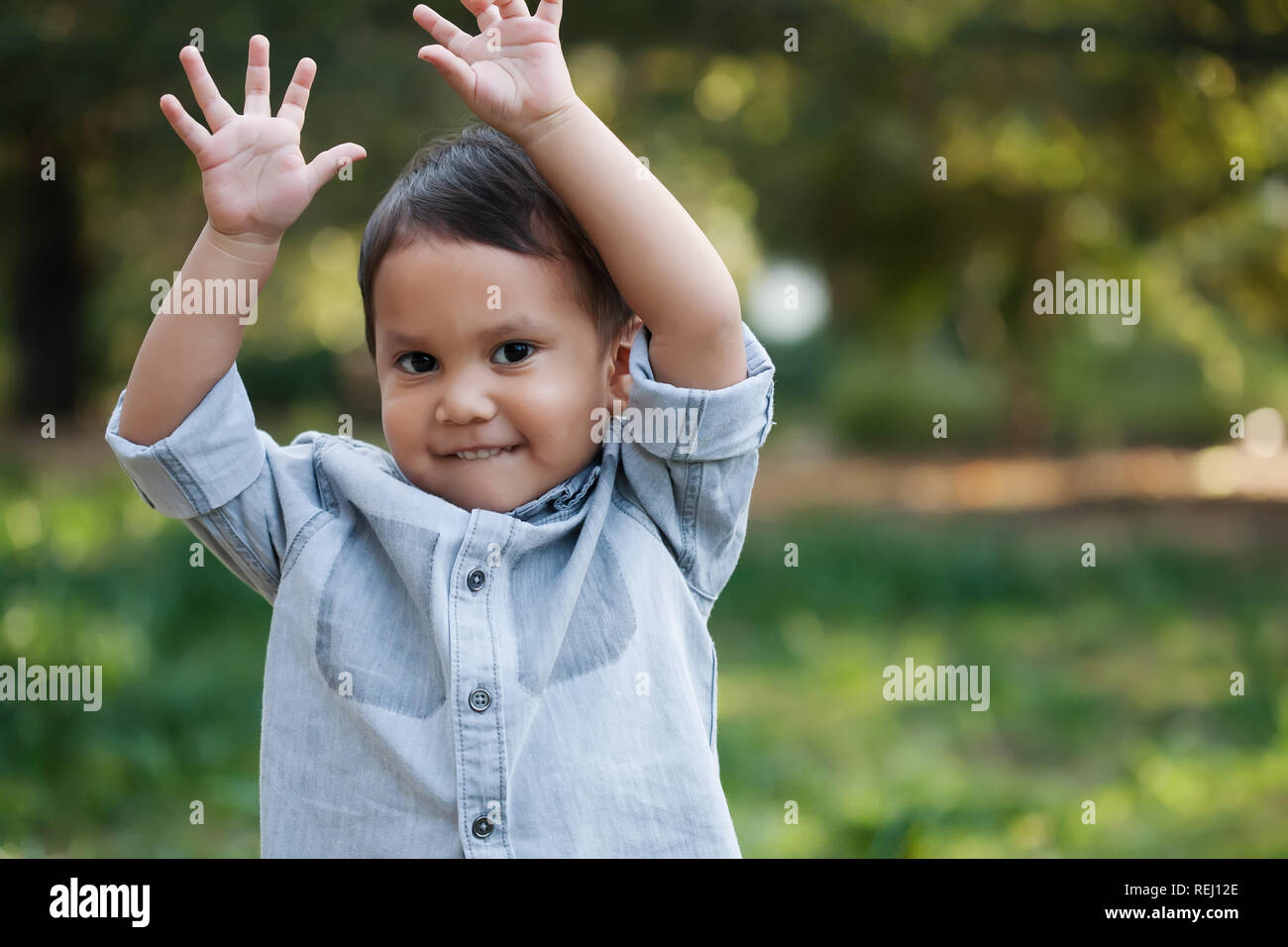 Un felice little boy sventolare le mani in aria, mentre in piedi in un giardino verde durante la primavera. Foto Stock
