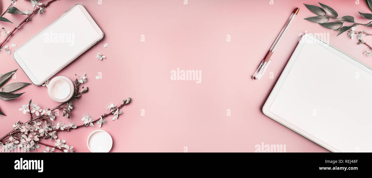 Smartphone e tablet pc mock up sul rosa pastello lo sfondo del desktop con cosmetici, articoli di cartoleria supples e fiori bianchi rami, vista dall'alto. Beaut blog Foto Stock