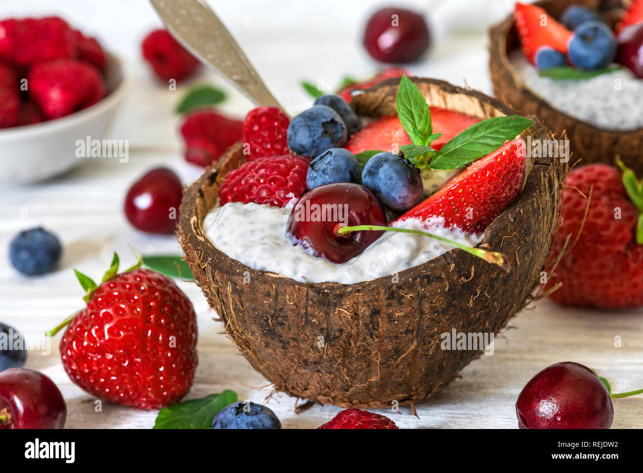 Budino di chia con frutti di bosco freschi, dadi, avena e menta in ciotole di noce di cocco con un cucchiaio. Colazione sana. close up Foto Stock