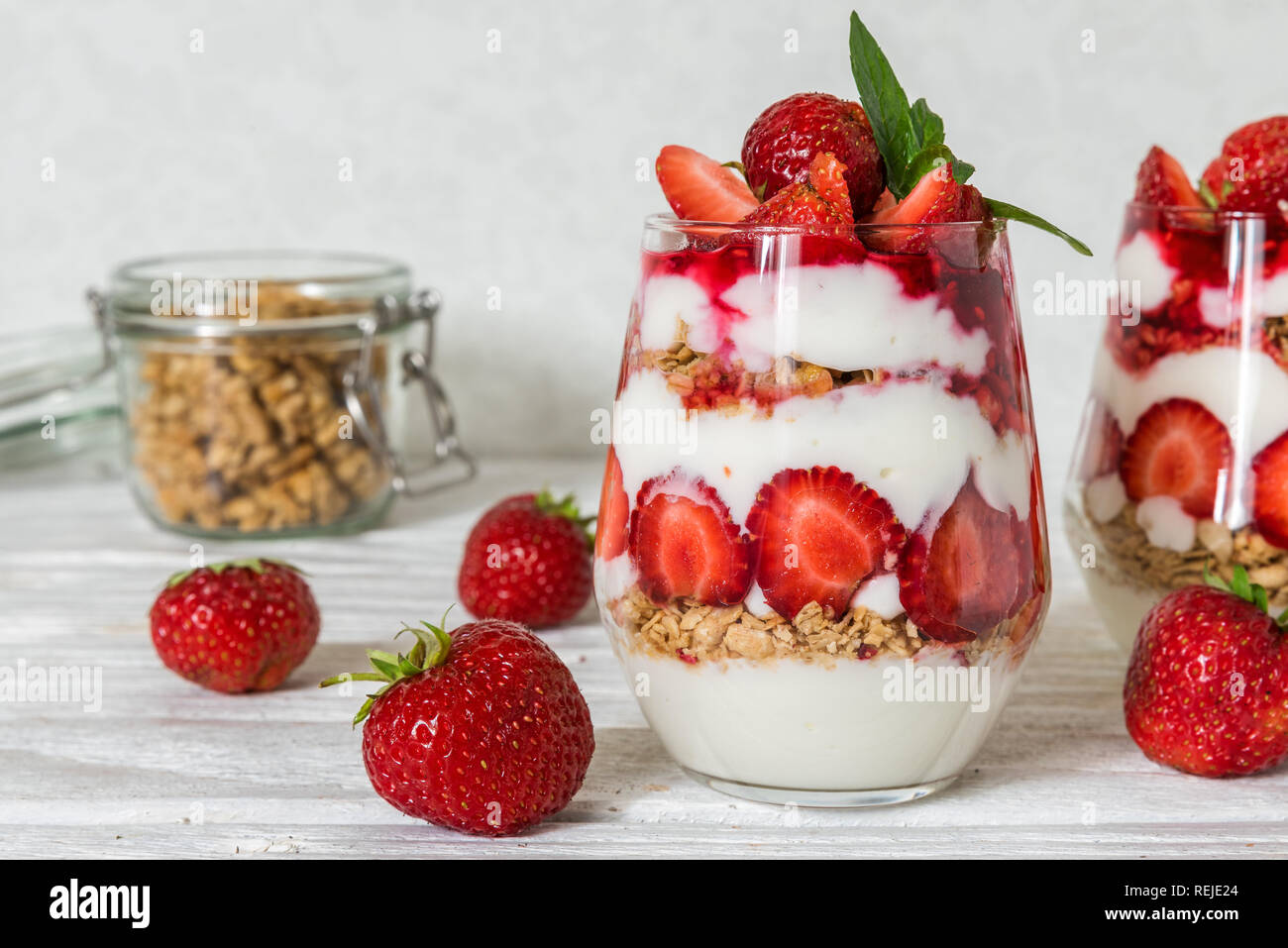 Yogurt fatto in casa parfait con granola e fragola in bicchieri bianco su un tavolo di legno. una sana prima colazione Foto Stock