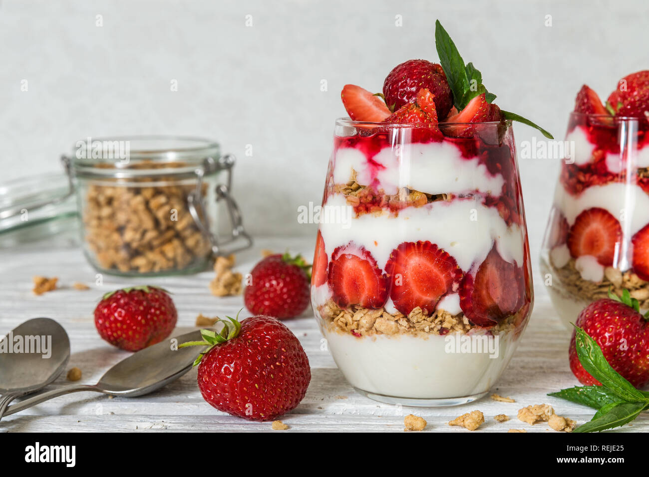 La frutta sana parfait di yogurt con muesli, menta e lamponi freschi in bicchieri bianco su un tavolo di legno. una sana prima colazione Foto Stock