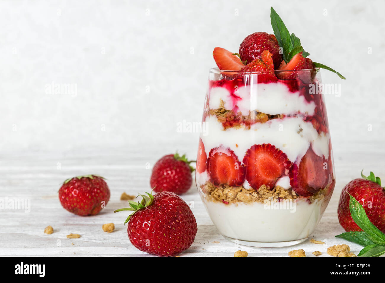 Yogurt fatto in casa parfait con granola e fragola in un vetro bianco su un tavolo di legno. una sana prima colazione Foto Stock