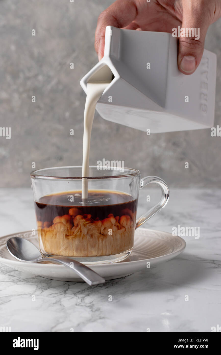 La crema versando in caffè con panna volute Foto Stock