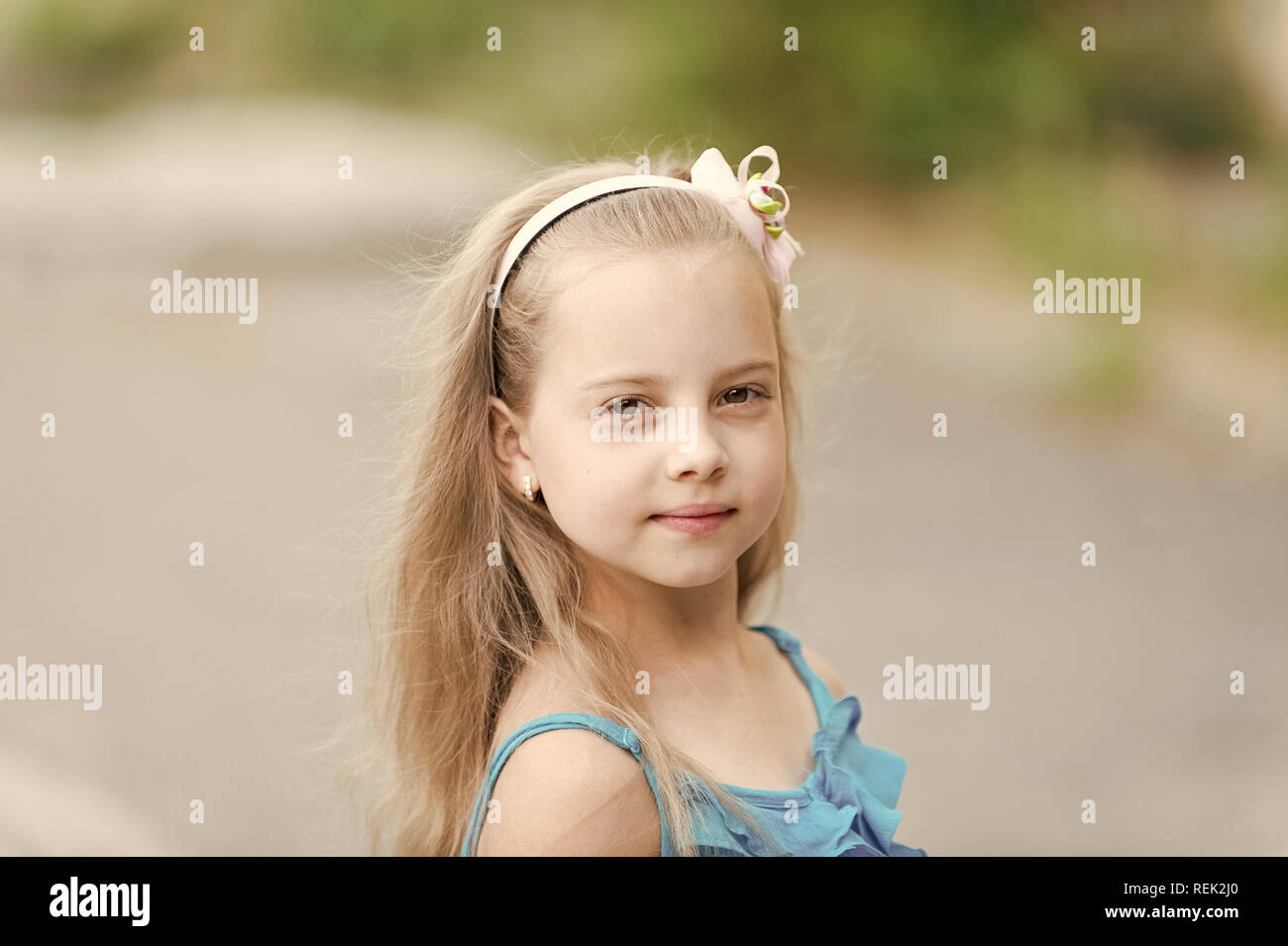 Piccola bambina o bambino carino con volto adorabile e archetto in capelli biondi nel giubbotto blu outdoor su sfondo sfocato Foto Stock