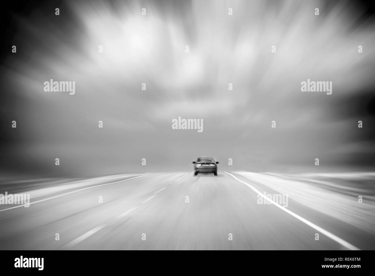 Vista posteriore di una vettura di accelerazione su strada asfaltata in campagna. Nuvoloso, cielo tempestoso. Immagine in bianco e nero con Copy-Space. Sfocatura del movimento Foto Stock