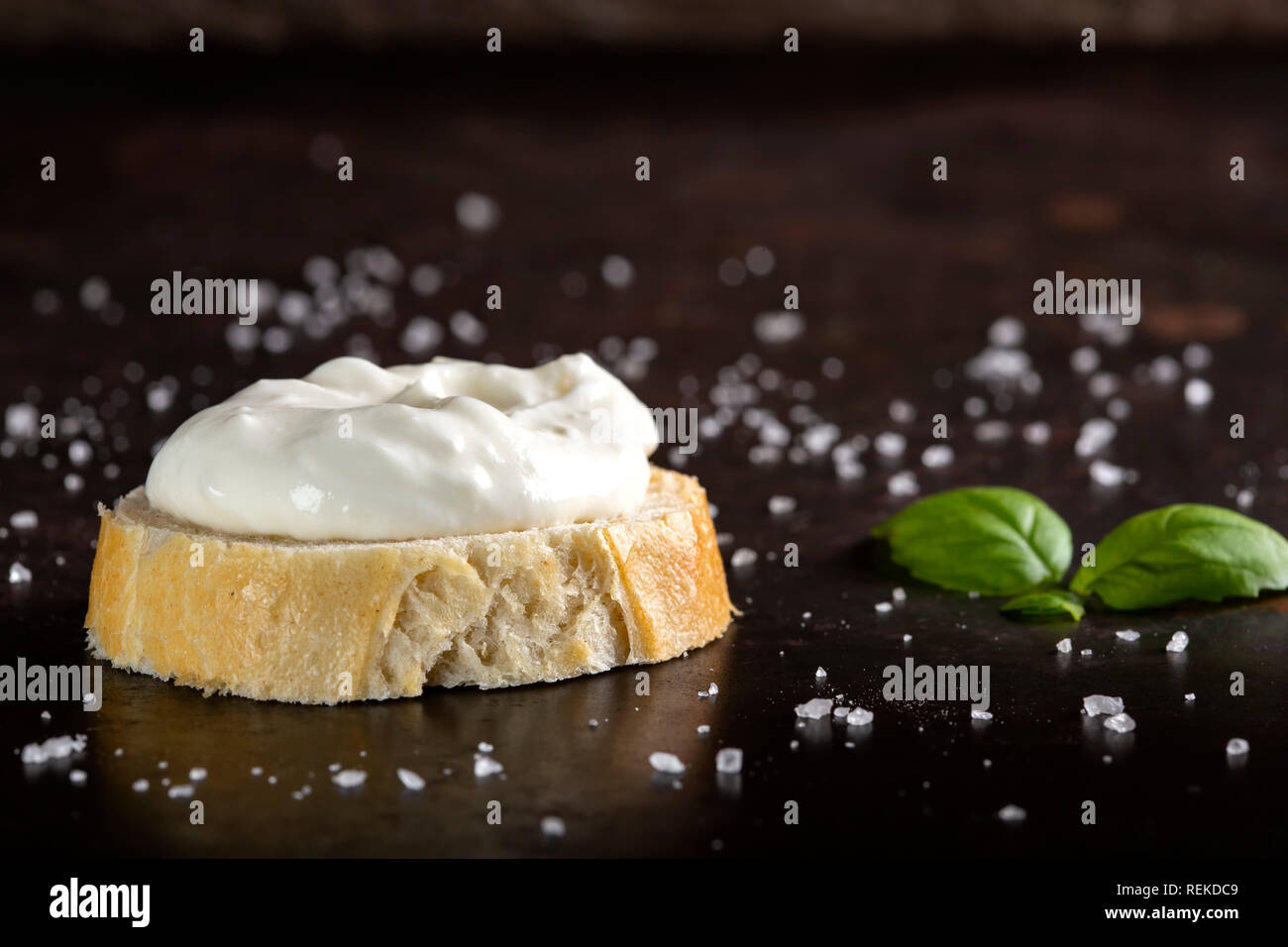 Una fetta di pane con salsa di panna e sale su uno sfondo scuro Foto Stock