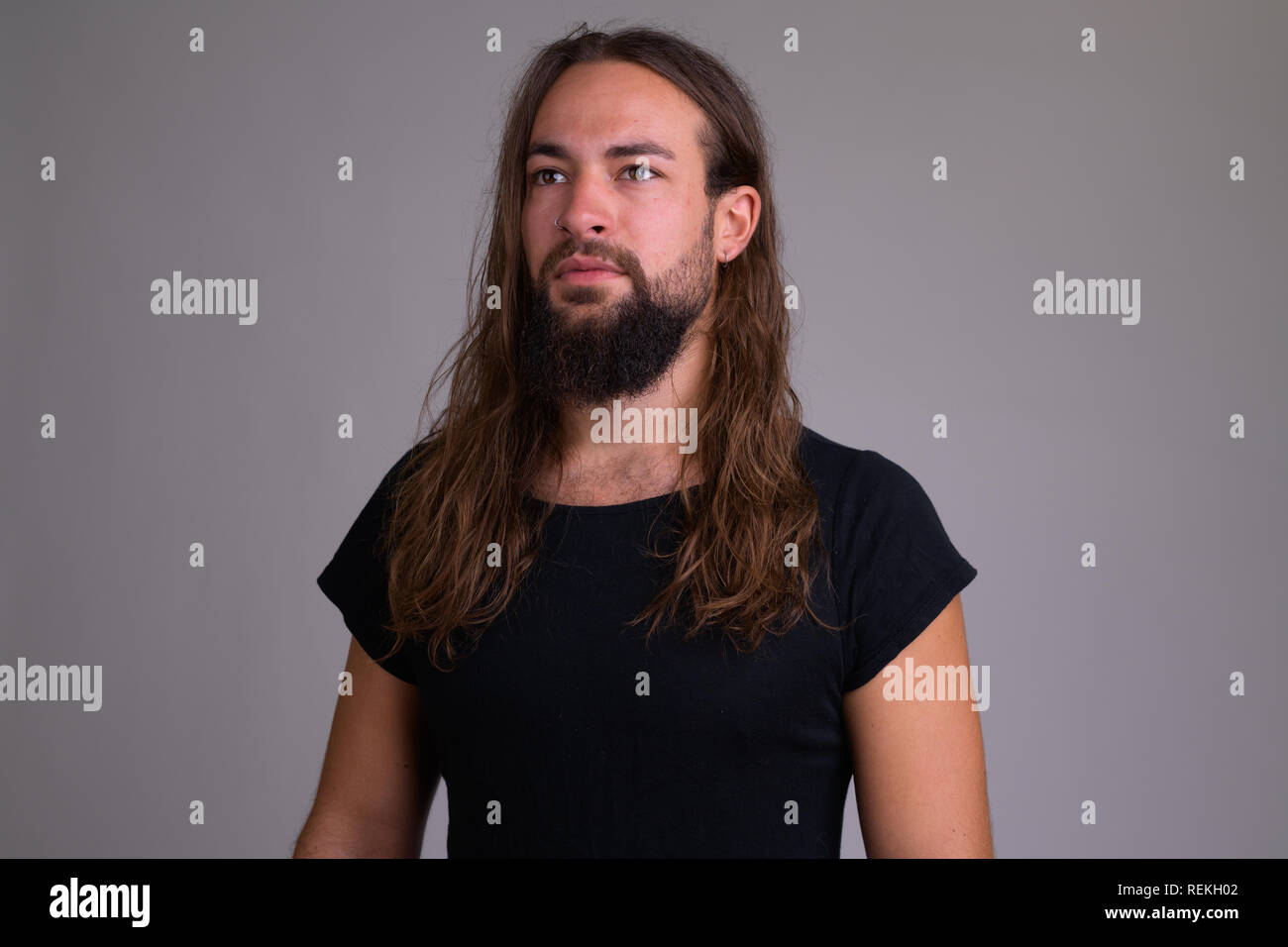 Bel giovane uomo barbuto con i capelli lunghi pensando Foto Stock