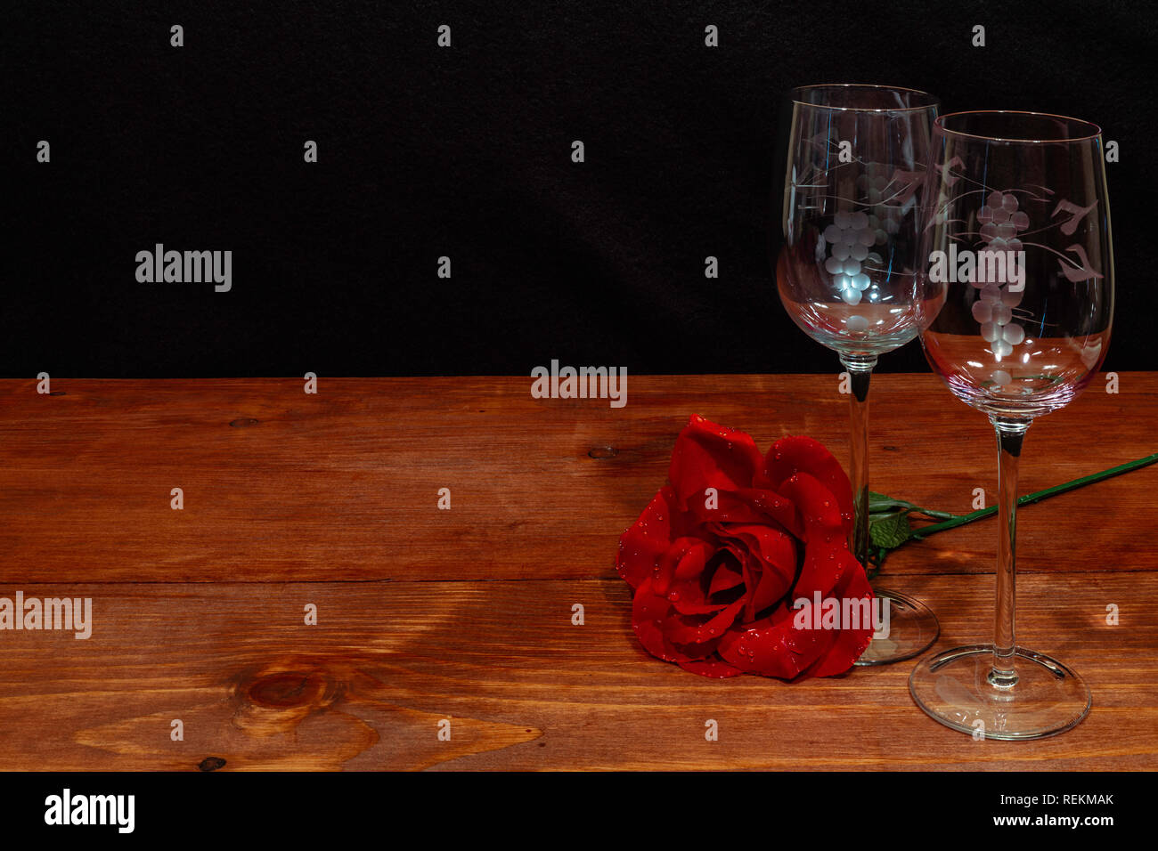 Bella inciso bicchieri di vino con una singola rosa rossa sul tavolo di legno e uno sfondo scuro. Valentines, Festa della Mamma, Pasqua, Natale, concetti di nozze Foto Stock