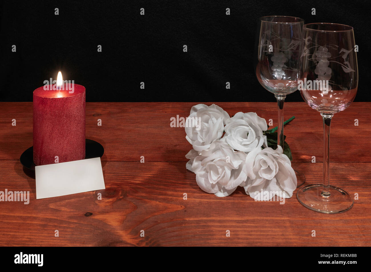 Bella inciso bicchieri di vino con awhite rose e candela rossa e il nome tag su un tavolo di legno e uno sfondo scuro. Valentines, Festa della Mamma, Pasqua, Chri Foto Stock
