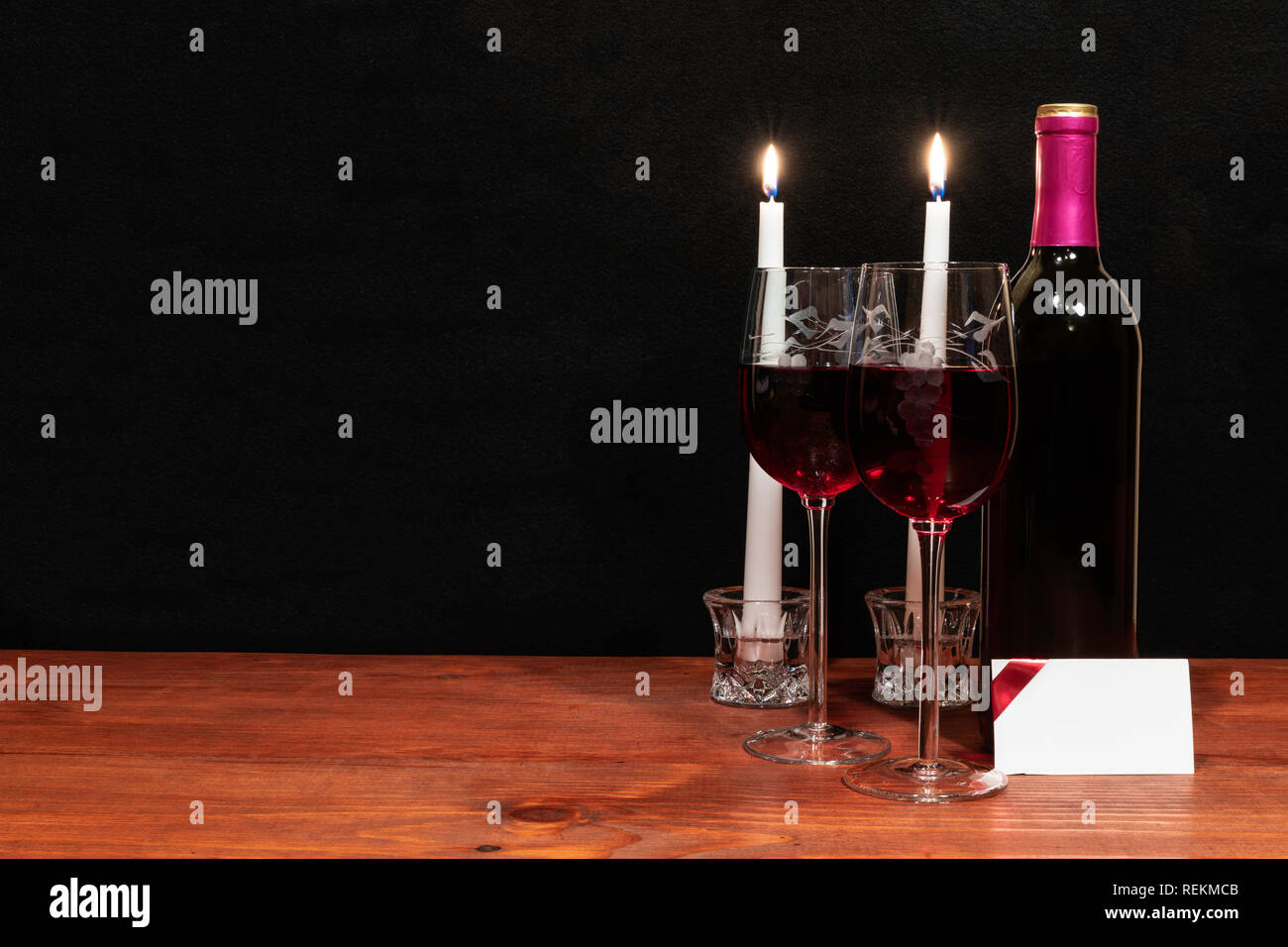 Bella inciso bicchieri di vino e una bottiglia di vino rosso, candele bianche, sul tavolo di legno con il nome di tag su sfondo scuro. Valentines, madri il giorno di Pasqua. Foto Stock