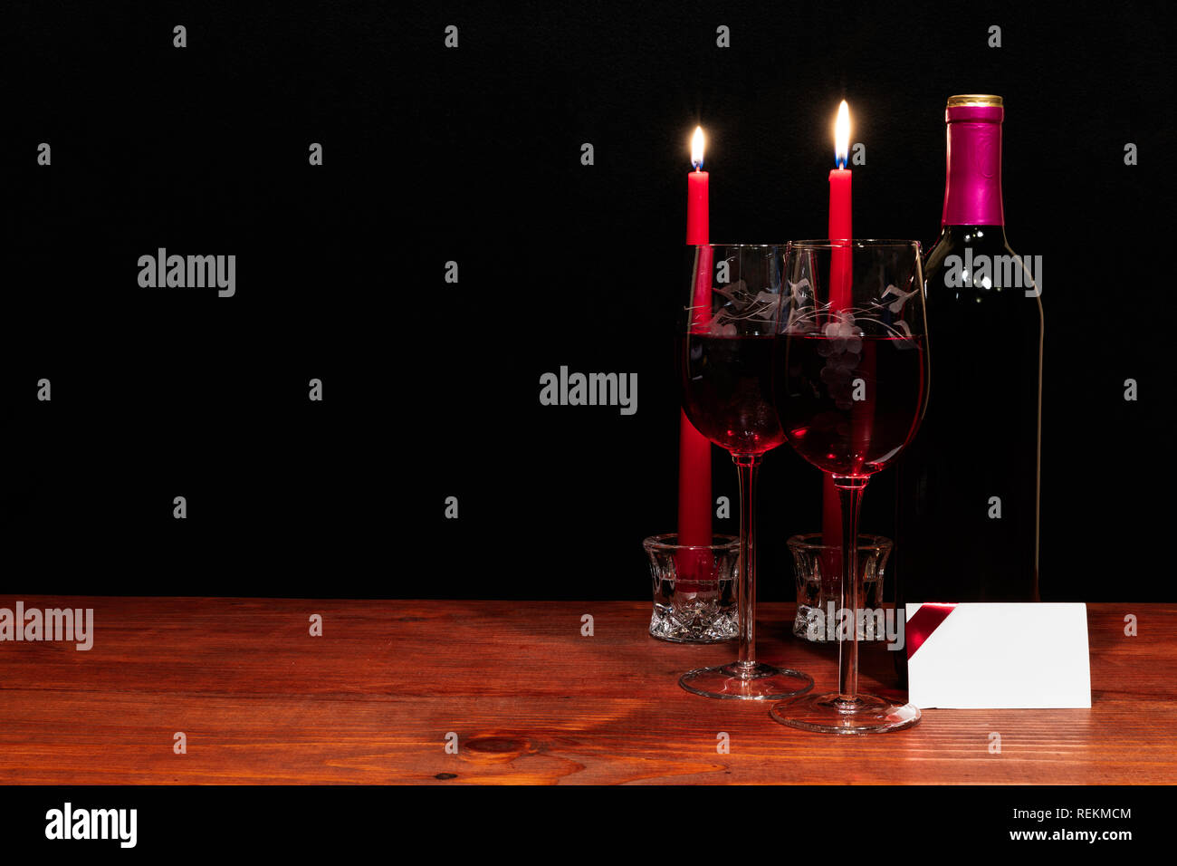 Bella inciso bicchieri di vino e una bottiglia di vino rosso, candele rosse, sul tavolo di legno con il nome di tag su sfondo scuro. Valentines, Festa della Mamma, Pasqua, Foto Stock